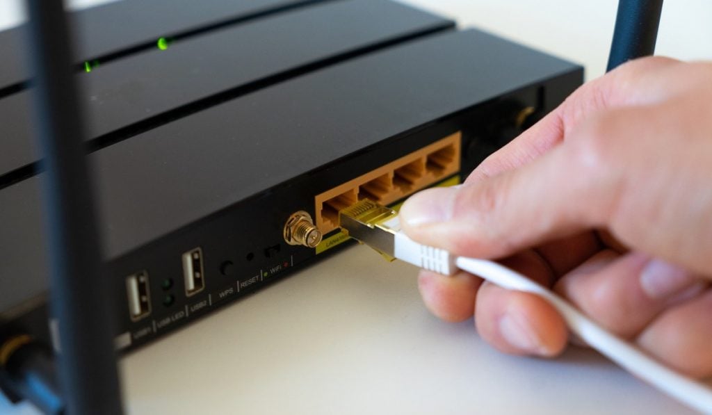 person plugging an internet cable into a black router
