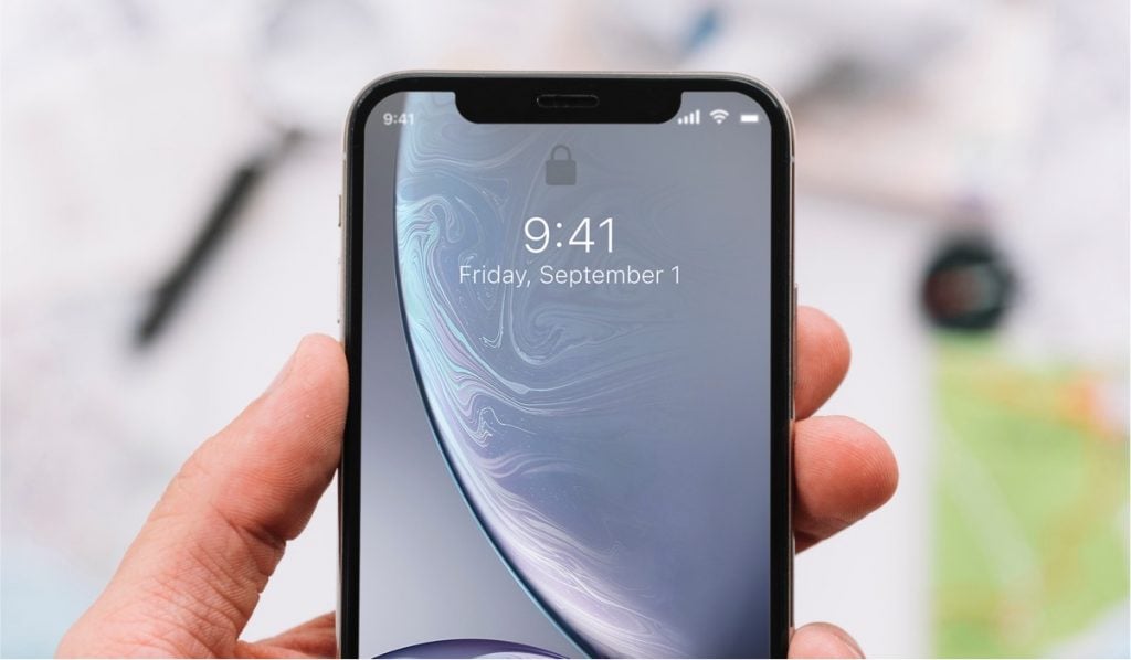 a hand holding an iPhone on a blurred background