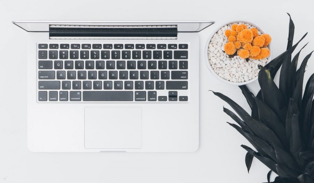 MacBook op een witte tafel met een ananas en een decoratieve schaal