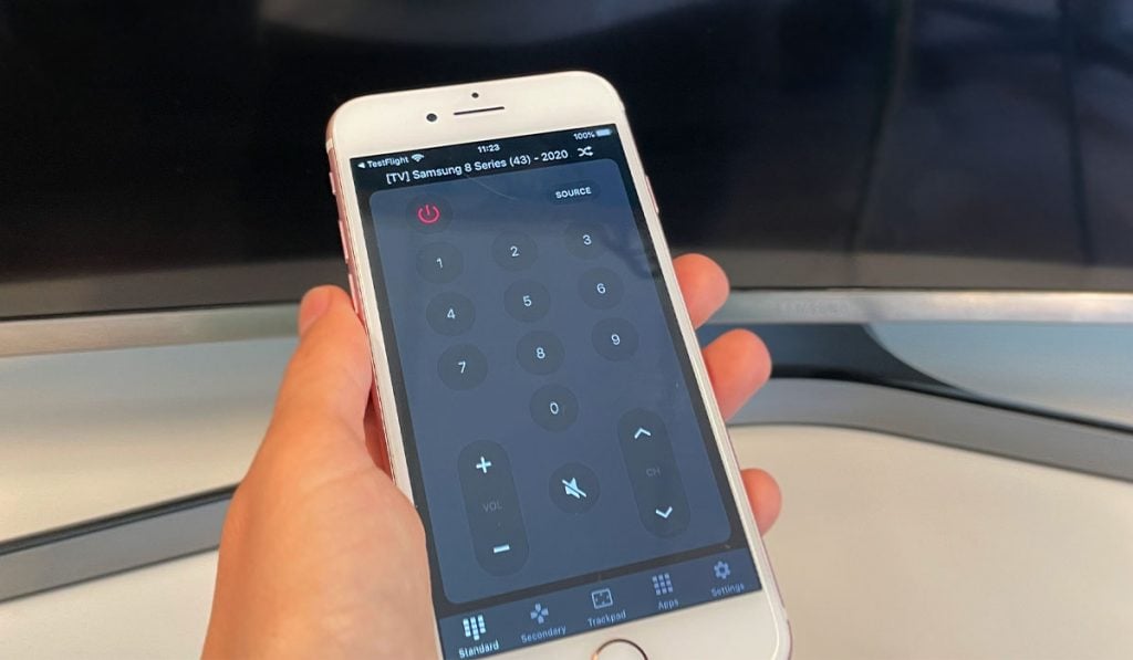 gros plan d'une personne vêtue d'un pull-over tenant un iPhone avec l'application ControlMeister devant une smart tv samsung