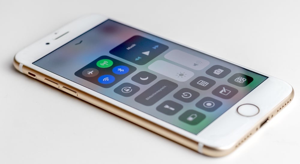 um iPhone branco com a sua interface mostrando o logótipo wifi, bluetooth e rede móvel e outros ícones rápidos no painel de controlo, sobre um fundo branco