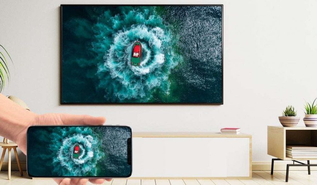 uma pessoa a espelhar uma imagem aérea de um barco de um iPhone para uma TV inteligente suspensa