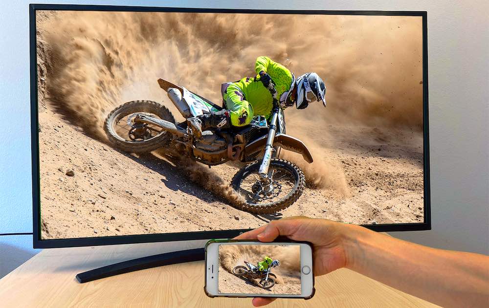  lo schermo di un iPhone che riproduce su una Smart TV l'immagine di un pilota su una moto da cross mentre la sabbia vola in giro
