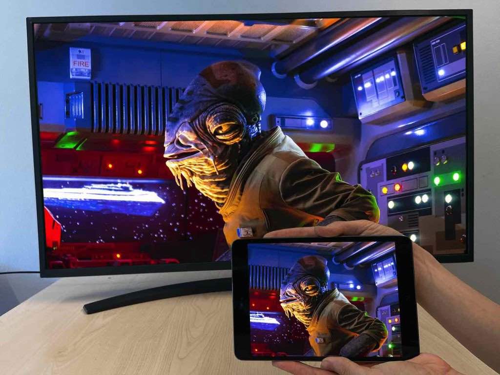 A hand holding an iPad that is casting an image of Admiral Ackbar from Star Wars to a Smart TV. The Smart TV is on a table 