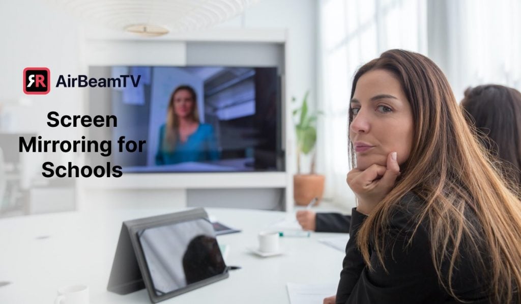 woman sitting in a clasroom looking backwards at a camera. In front of her is a Smart TV with a live stream of a lecture.