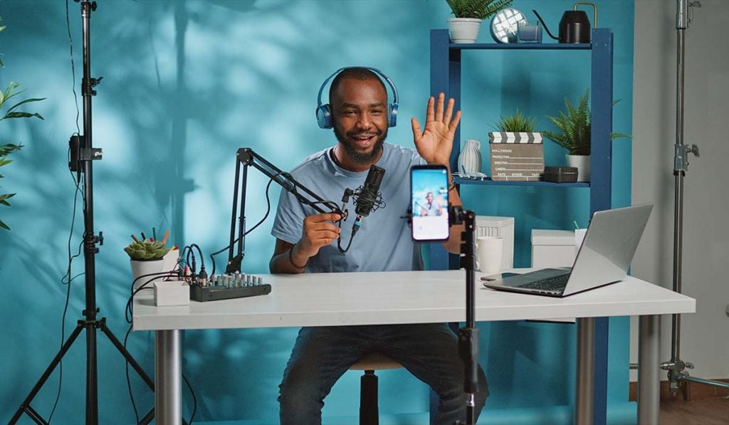 Um homem sentado perto de uma mesa em frente a um computador com fones de ouvido ao falar com um microfone
