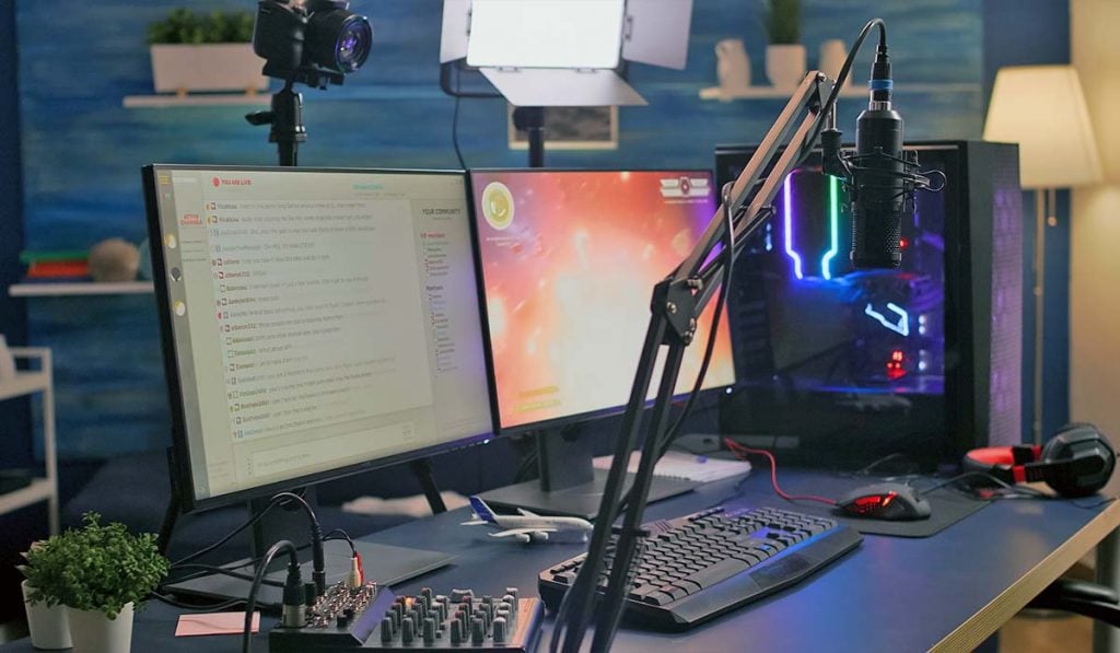een computeropstelling met een microfoon, een geluidsmixer, een toetsenbord en twee monitoren