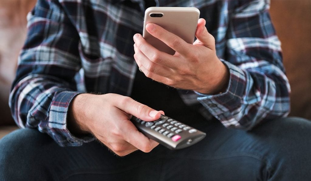 Man holding smartphone and remote control