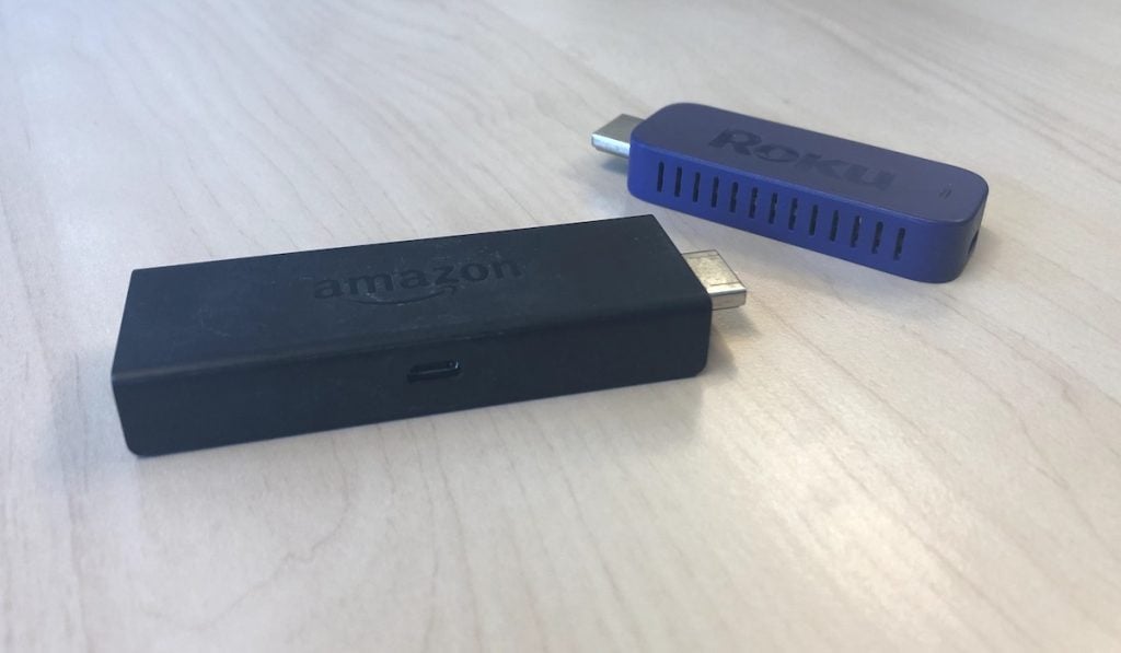 A Roku stick and a Fire Tv stick arranged on a wooden table