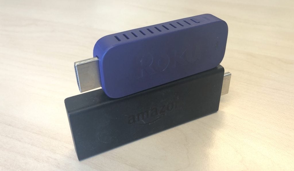 Roku Stick on top of a Fire Tv Stick. the fire TV stick stands on a wooden table