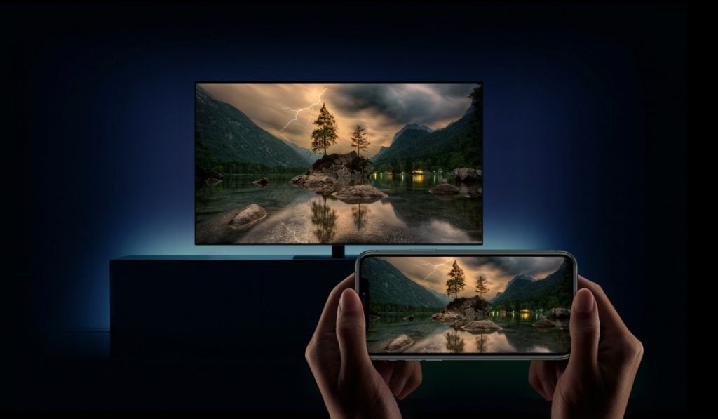 Woman mirroring the screen of a smartphone to a Smart TV standing against an illuminated wall