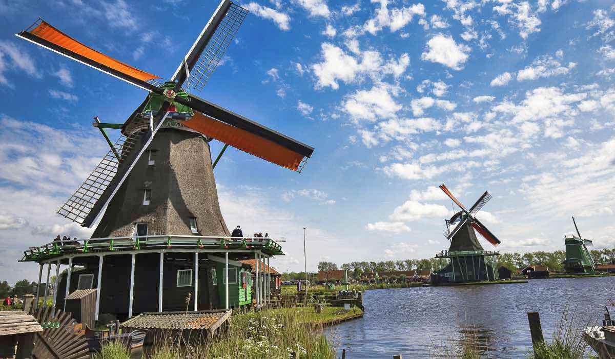 three dutch windmills on a sunny day next to a water canal