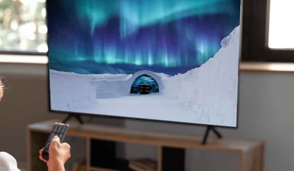an image of an igloo in a snowy landscape and Aurora Borealis displayed on a Smart tV. The TV stands on a television stand against a window
