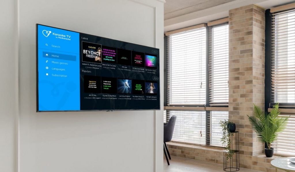 application karaoke tv sur une Smart TV Samsung accrochée à un mur avec deux fenêtres et plusieurs plantes à côté d'elle