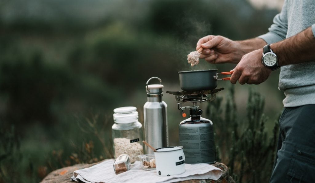 man cooking oatmeal on a gas stove in the wilderness