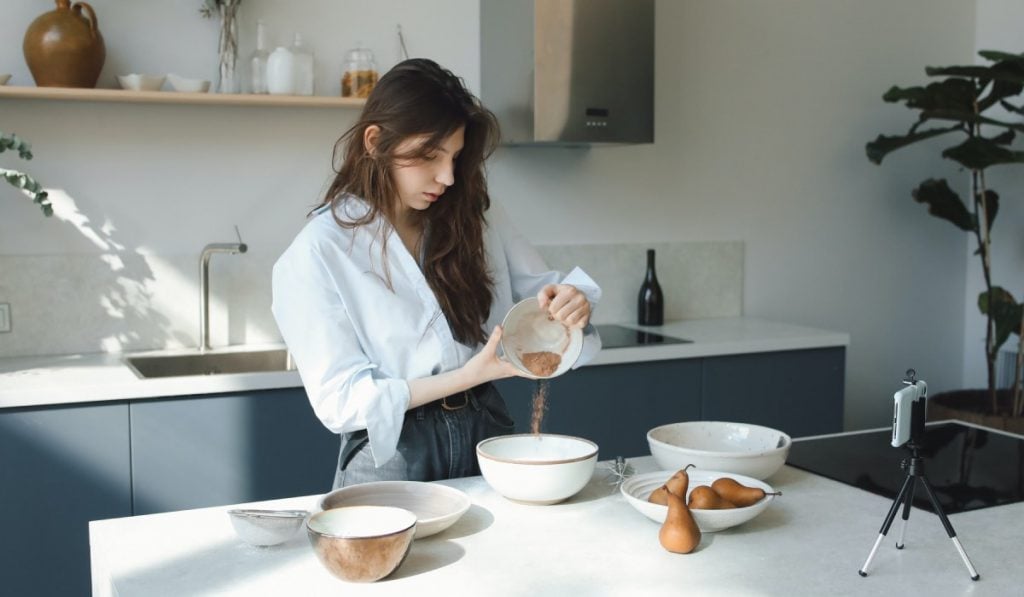 woman pouring spices from small bowl to a big bowl in a kitchen
