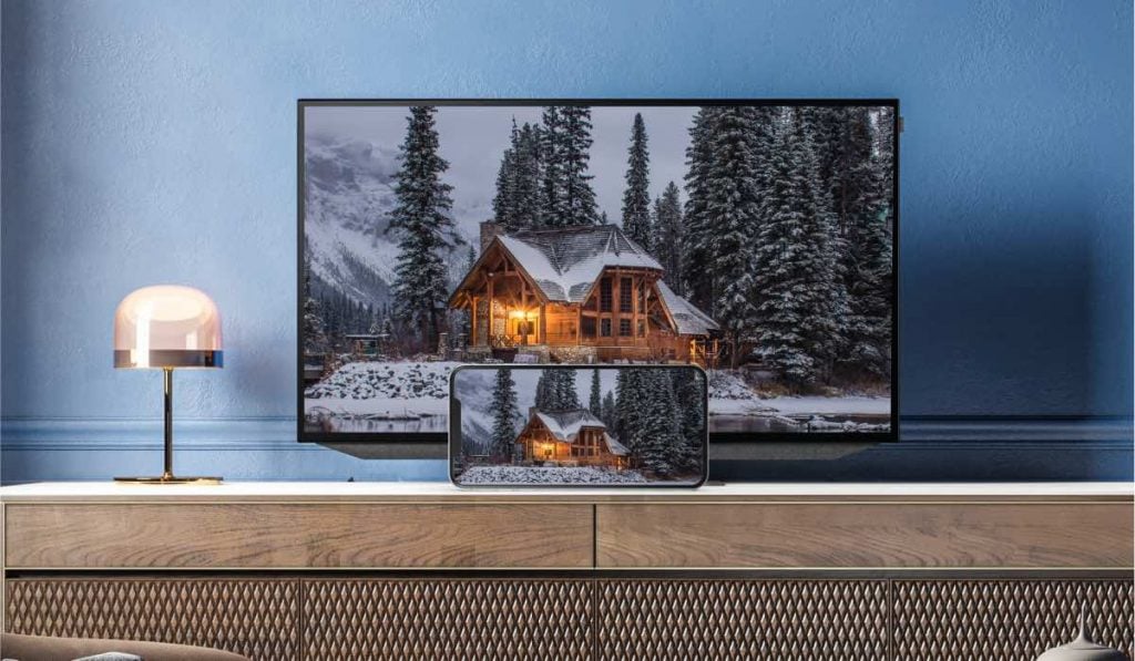 a smartphone casting an image of a snowy house with the lights on to a Smart TV