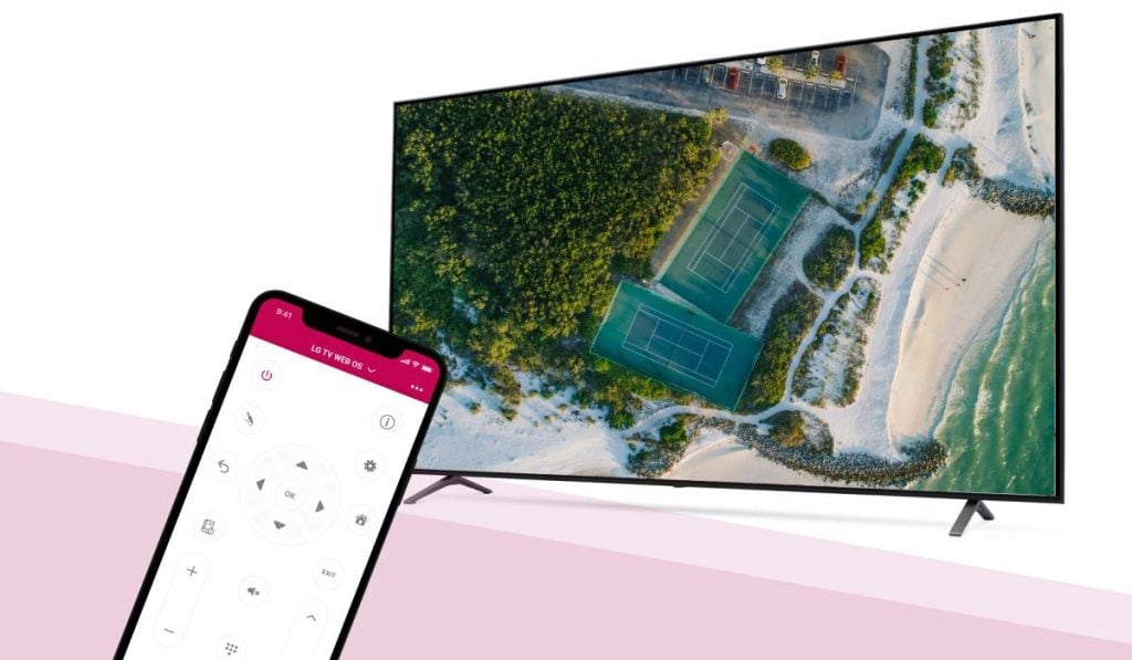 an iPhone with the LG TV remote app by MeisterApps on the screen pointed at an LG Smart TV. The LG Smart TV has an image of a bird's eye view of two tennis pitches, a forest, a beach and a parking