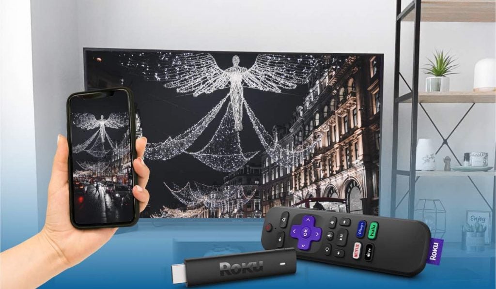 Roku stick and a Roku remote, a hand holding a smartphone that casts an image of Christmas street decorations