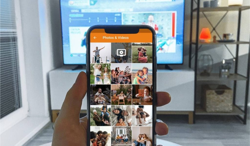 A hand holding a smartphone open on the gallery app. There's a Smart TV in the background