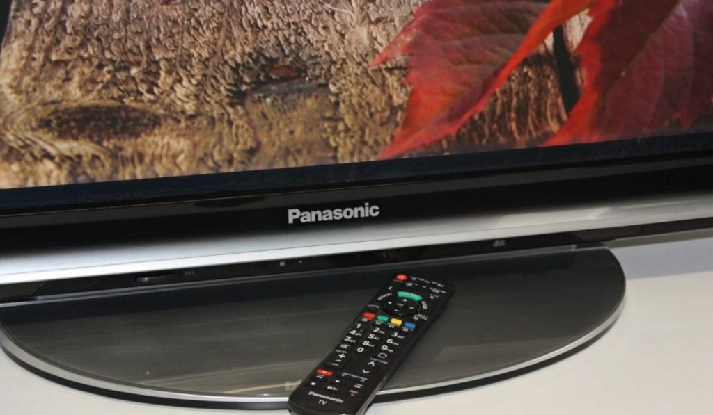 A bottom of a Panasonic TV with a remote laying at the base.