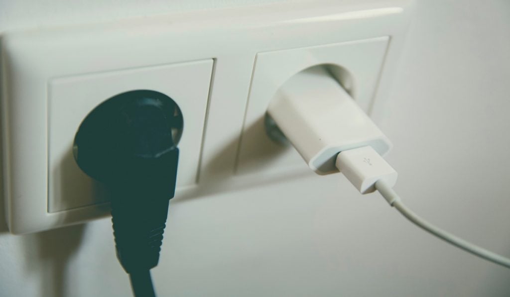 Two power sockets, one with a black power cable and the other with a white phone charger.