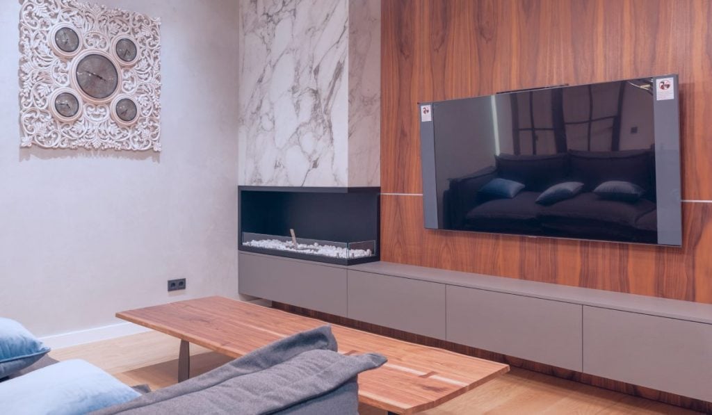 Samsung TV hanging on a wooden wall. There's an aquarium next to the TV. There are couches and a coffee table in front of the TV