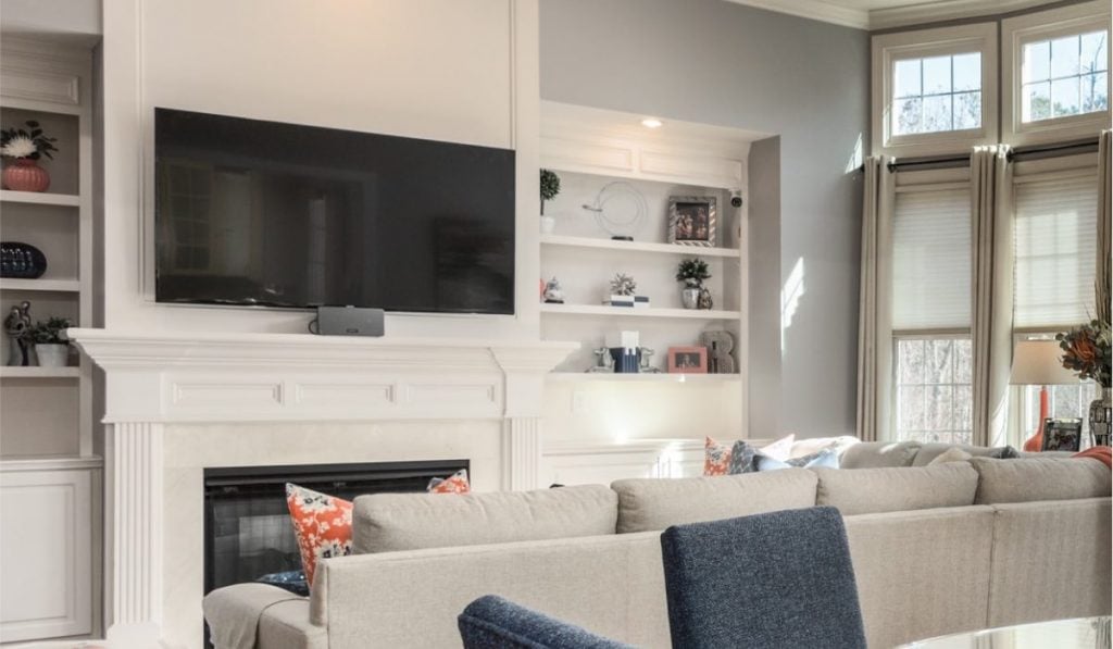 A Samsung TV hanging on a wall with a soundbar attached to it. There's a mantlepiece below the TV and a kitchen in the background.