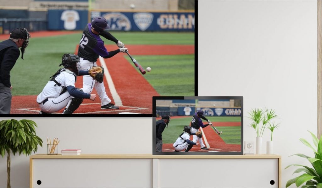 A tablet casting an image of baseball players to a TCL TV. The tablet is resting on a drawer, the tV is hanging on a wall.