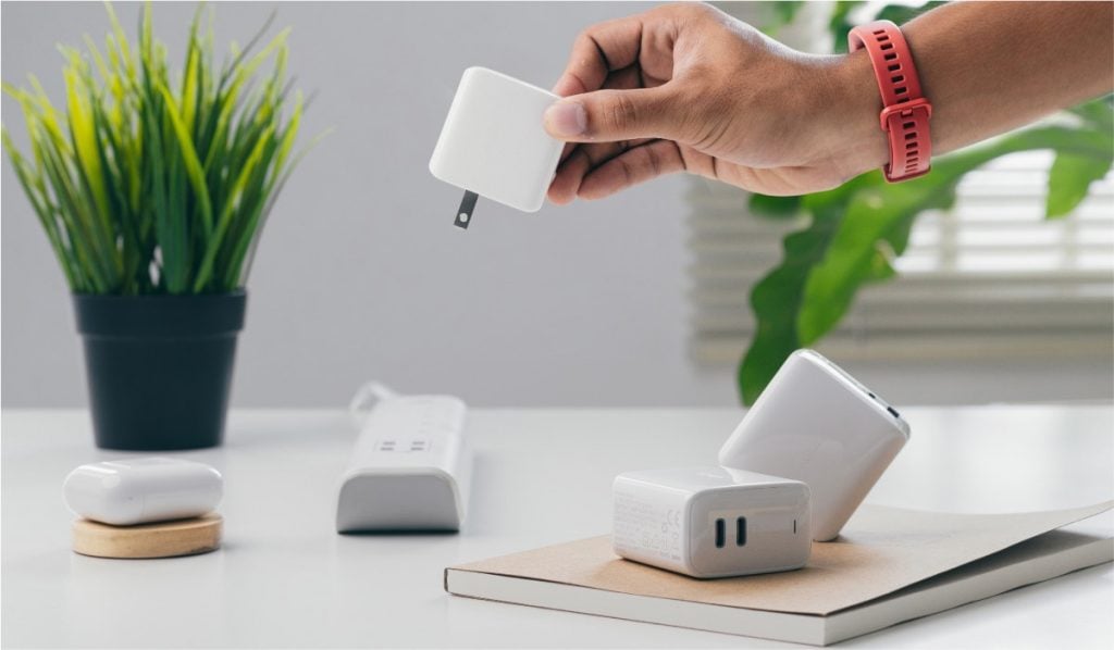 Various charger cubes on a table. There's a hand picking up one of the cubes and a plant on the table