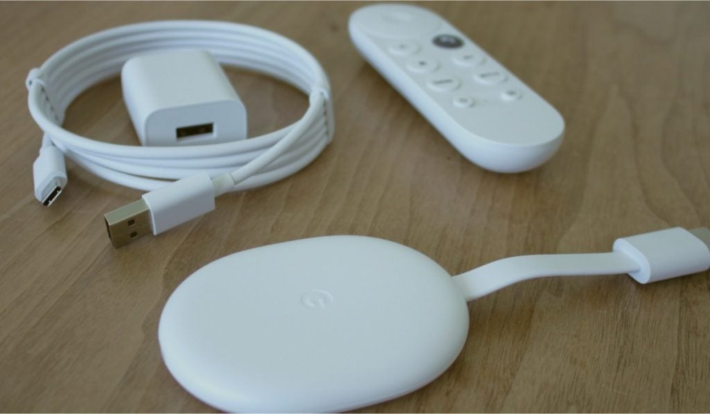 A power cable, an adapter, a Chromecast remote and a Chromecast device on a wooden surface