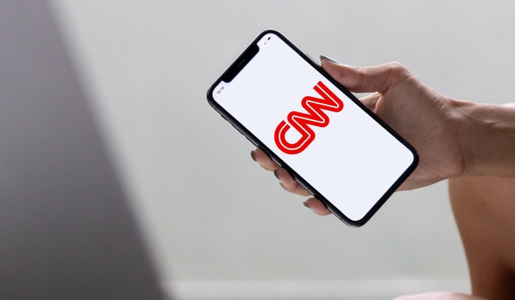A hand holding a smartphone with the CNN logo on the screen.