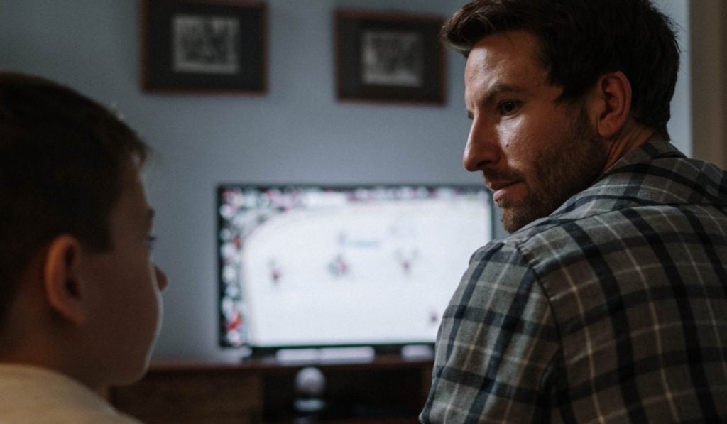 Father and son look at each other. There's sports on TV