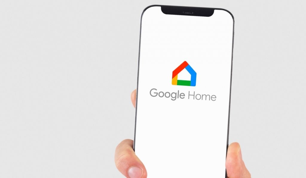 A hand holding a smartphone with the Google Home app logo on the screen