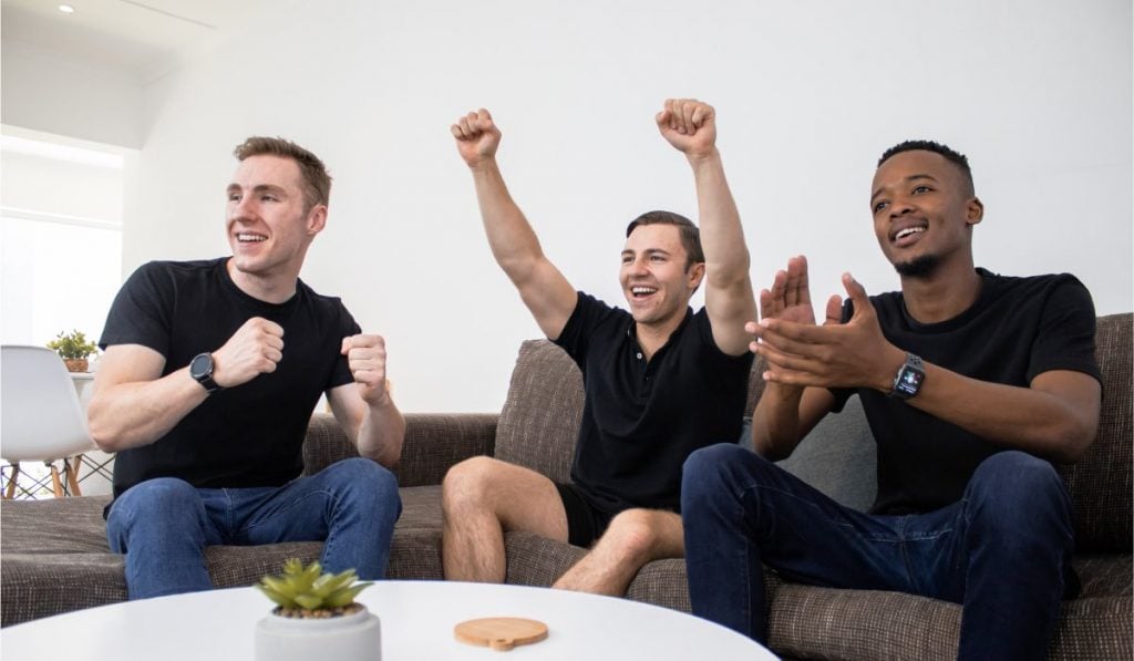 Three men are sitting on a couch and cheering.