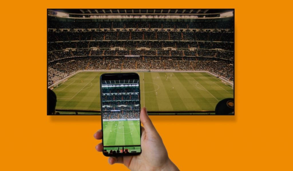 a hand holding a smartphone that is mirroring an image of a football pitch to a TV