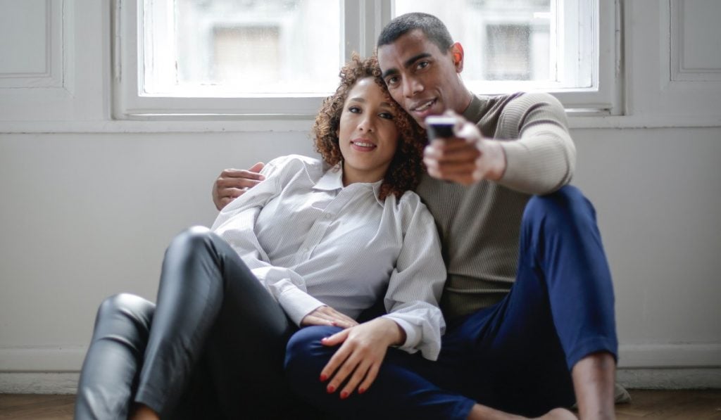 A man and a woman sitting in an embrace. The man is holding a remote control.