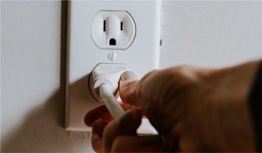 An image of a white double power socket with a hand plugging in a white cable into the bottom socket.