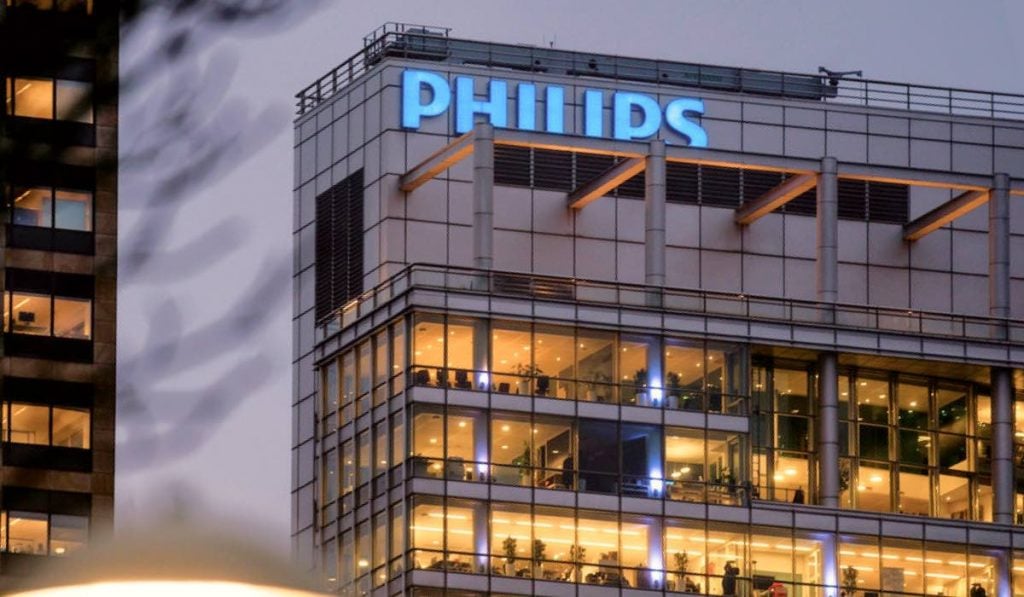Philips office building with lights on. The weather is cloudy. There's another building to the left.