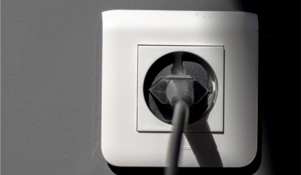A closeup image of a white power socket with a black power cable plugged in