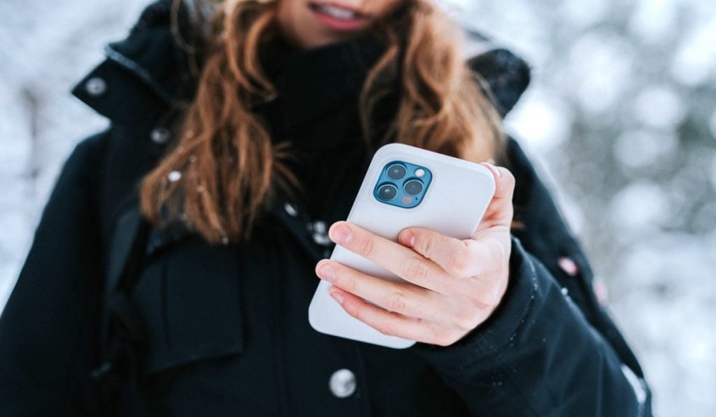A woman in a black coat using a white iPhone in a snowy landscape
