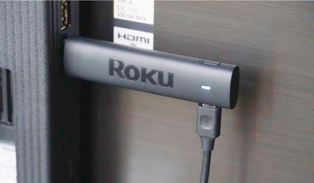 A Roku Stick plugged into an HDMI socket on a Smart TV. The Roku Stick is plugged into a USB-C power cable
