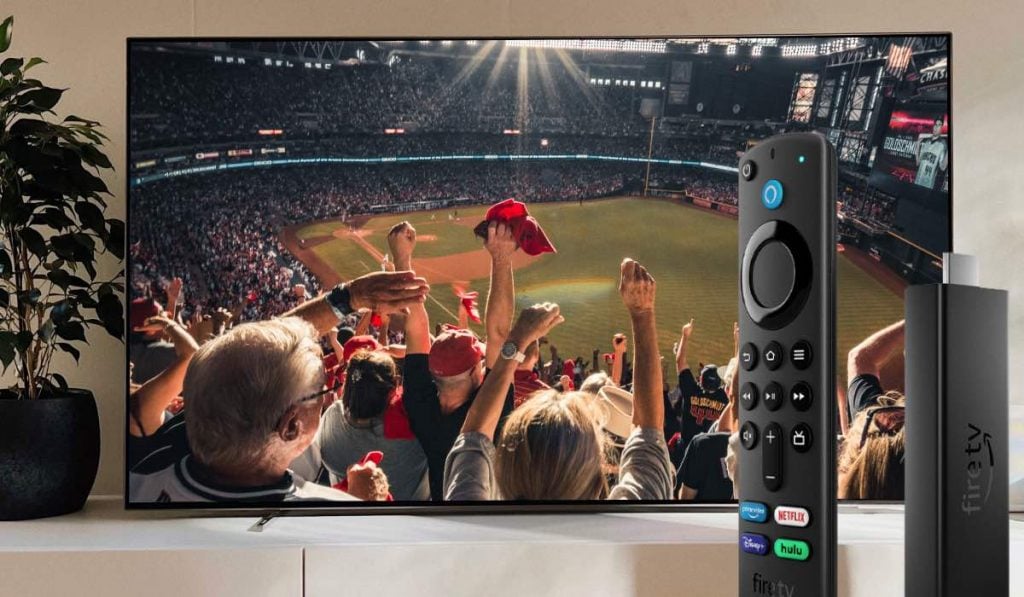 A Smart TV displaying a football match with supporters cheering. A Fire TV stick and a Fire TV remote