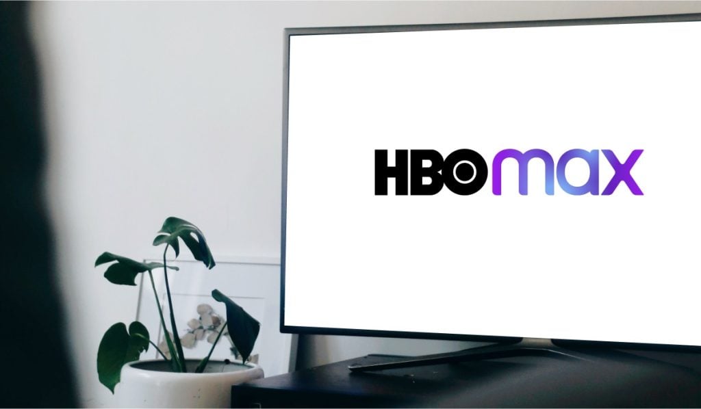 A TV with an HBO Max logo on the screen. The TV is standing on a black drawer with a monstera plant next to it.