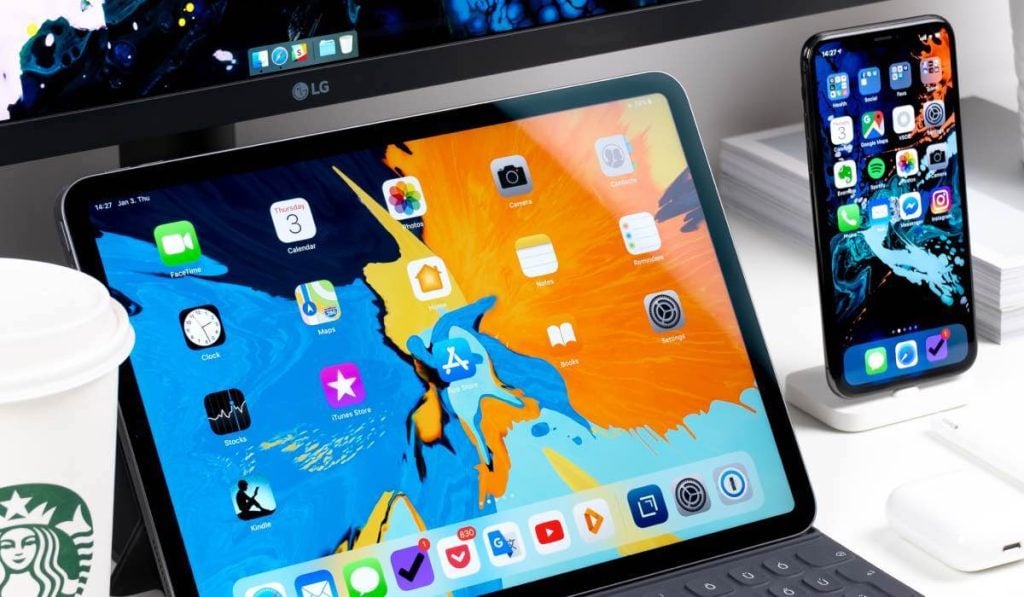 A MacBook and an iPhone on a desk. Both have the app launcher menus on the screen