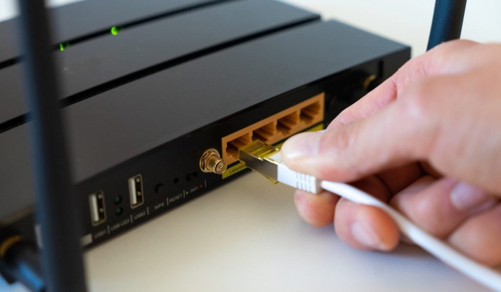 A hand plugging in a network cable to a black router