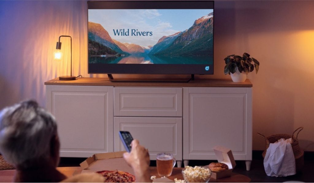 A hand holding a remote control pointing it at a TV with Wild Rivers on the screen