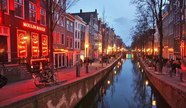 a canal in Amsterdam in the evening with lights and trees