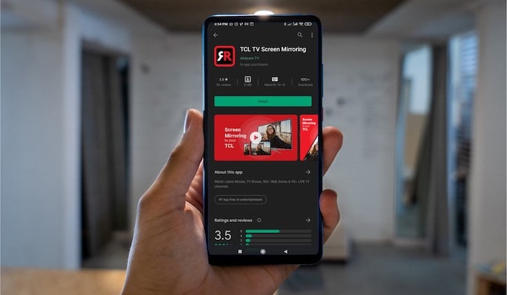 A hand holding an Android phone with the Google Play Store page for TCL TV Screen Mirroring on the screen