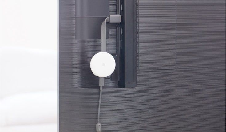 White Chromecast device plugged to the back of a Smart TV. The Chromecast device is plugged to a USB-C power cord.
